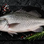 barramundi bali – whole fresh barramundi on slate board with salt and rosemary