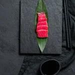 Tuna saku sashimi Bali — tuna slices on a bamboo leaf on a black slate board