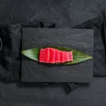 Tuna sashimi Bali — sliced tuna saku on a bamboo leaf with soy sauce and chopsticks